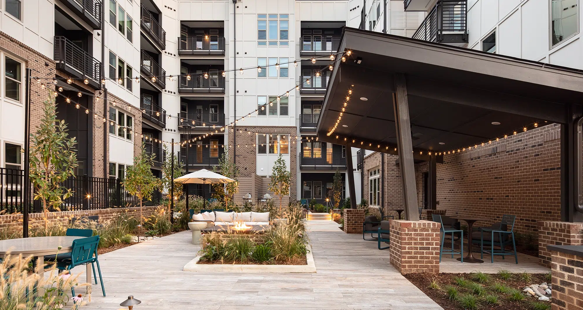 Modern apartment courtyard featuring string lights, lush greenery, and a communal gathering space